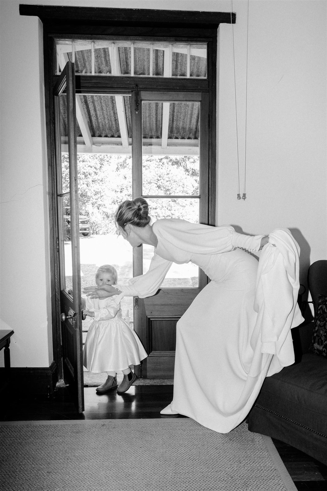 Black and white: a bride bending down to a little girl in a white dress at an open doorway