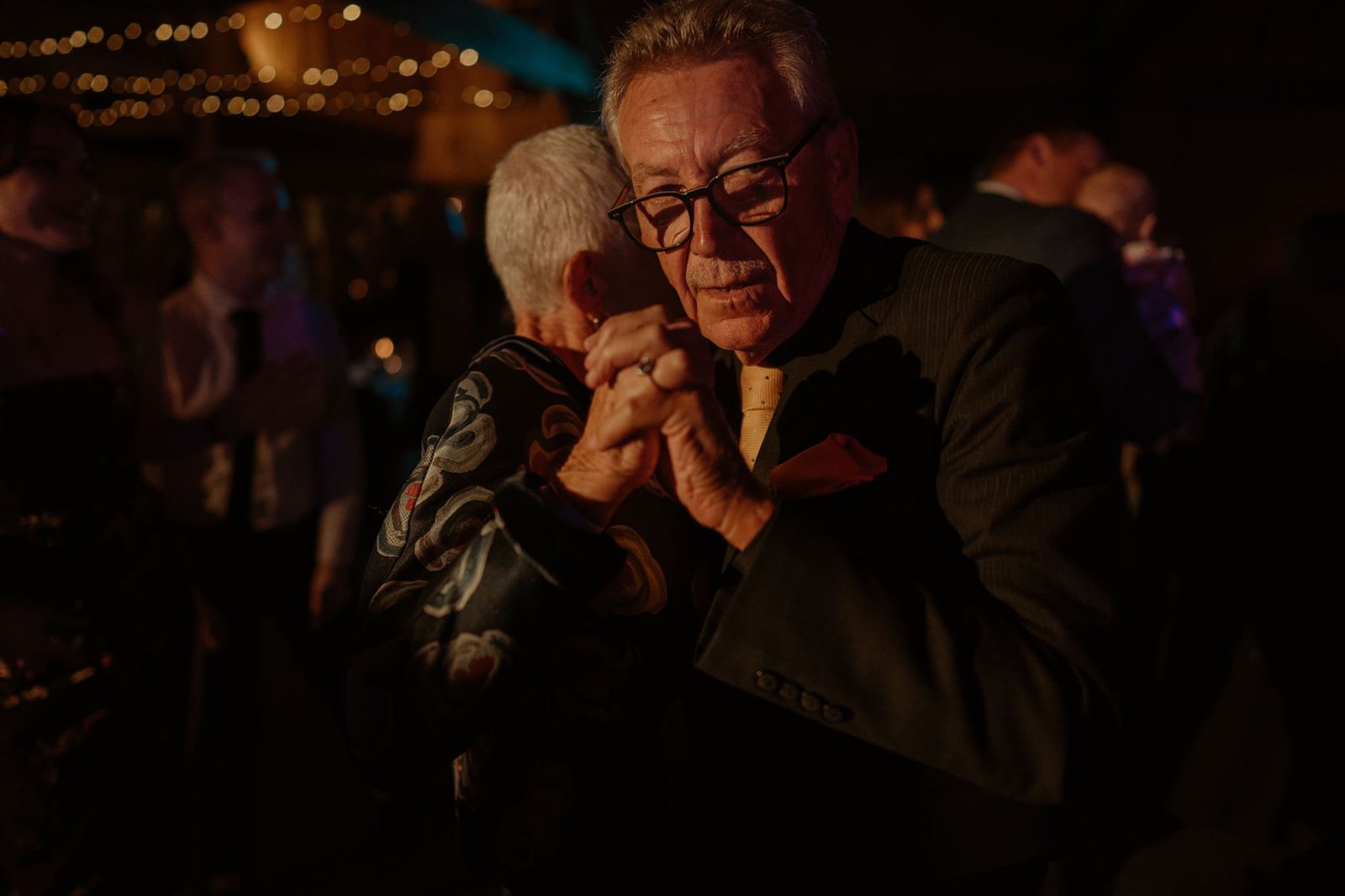 An older couple slow dancing cheek to cheek under festoon lights
