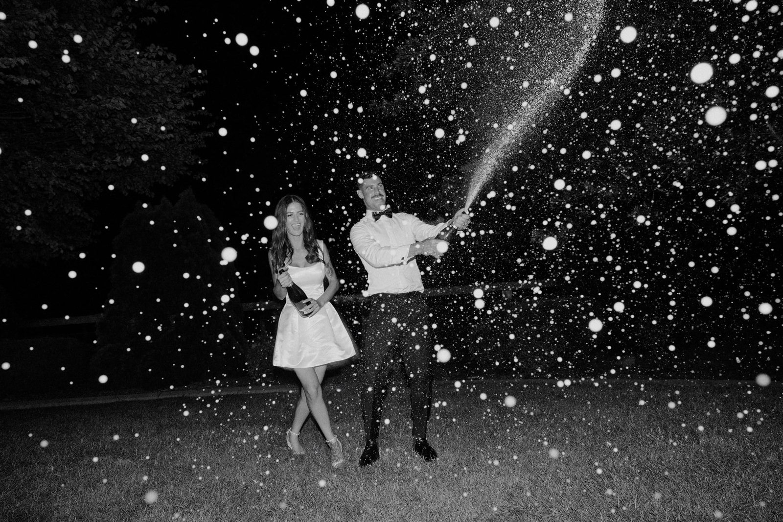 Black and white: a couple laughing at night as sparkles spray across the frame