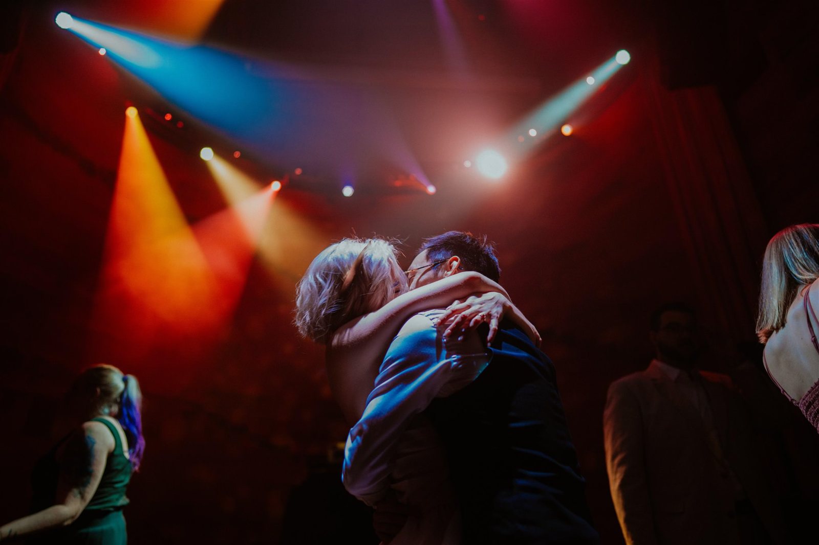 A couple dancing close under red and blue stage lights