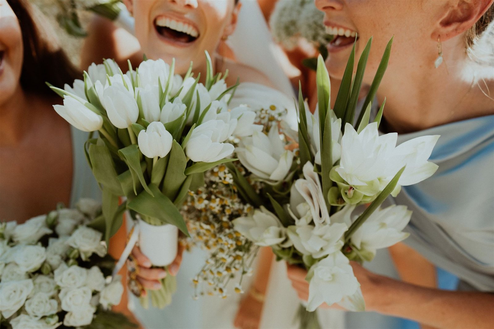 White tulips and roses held between two laughing bridesmaids