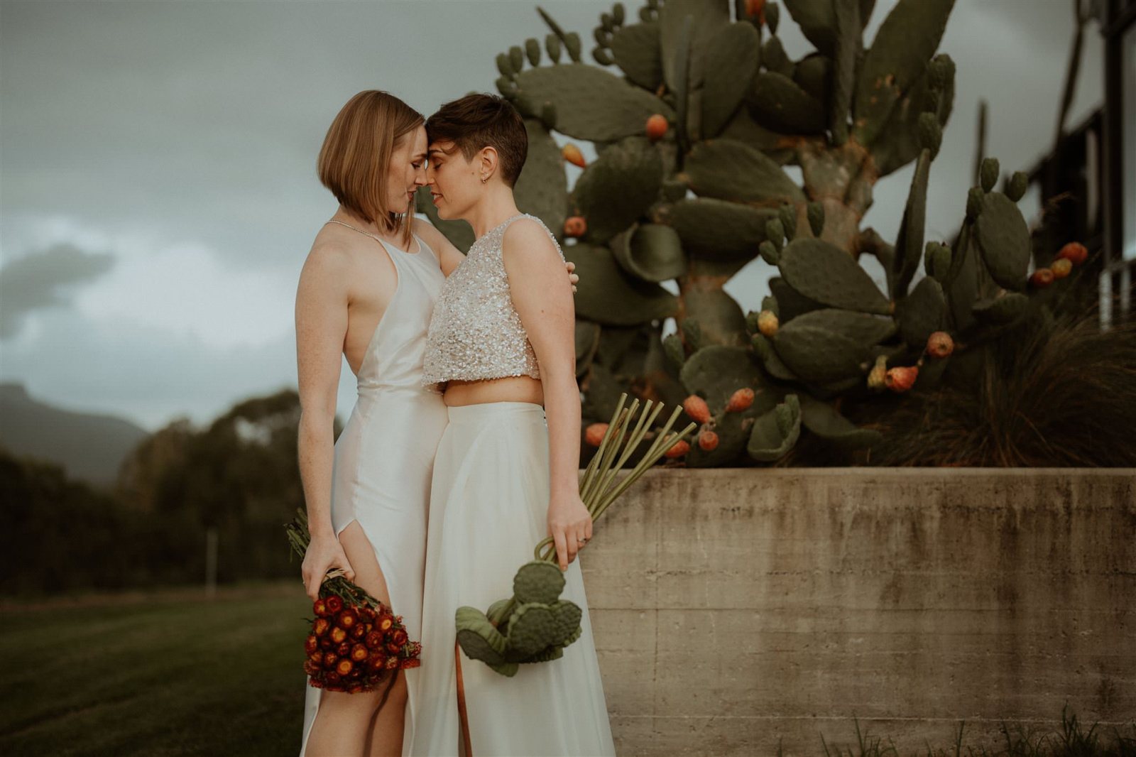 Two brides foreheads together beside a cactus garden
